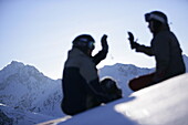 Young man and woman sitting on snow, clapping hands, Kuehtai, Tyrol, Austria