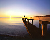Man relaxing at end of wooden jetty, sunset, St. Heinrich, Upper Bavaria, Germany