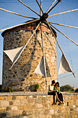 Two women sitting in front of a windmill and reading a book, Antimachia, Kos, Greece