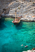 People swimming in a bay of Kalymnos next to a sailing boat, Greece