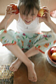 Girl holding apples to ears, laughing