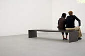 Couple sitting on bench in museum, Pinakothek der Moderne Munich, Bavaria, Germany