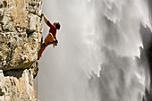 Frau klettert eine Felswand hoch, vor einem Wasserfall, Gelber Wahn 7b+, Kärnten, Österreich