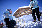 Woman pulling children in toboggan on snow, Brixen im Thale, Tyrol, Austria