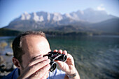 Man looking with binocular over Lake, Eibsee, Zugspitze in backround, Bavaria Germany