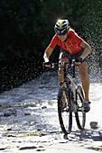 Mountainbikerin fährt durch Wasser, Oberammergau, Deutschland