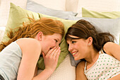 Two teenage girls (14-16) lying on bed in a whisper