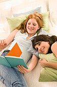Two teenage girls (14-16) lying on bed looking into book