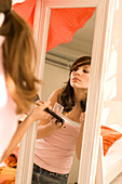 Teenage girl (14-16) applying make-up in mirror, sideview