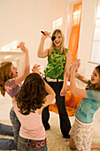 Girl (14-16) singing into make-up brush, three girls clapping hands