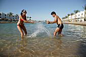 Young couple splashing each other in sea, laughing