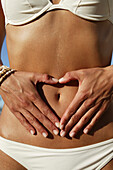 Woman with fingers forming heart around navel, close-up