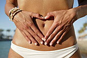Woman with fingers forming heart around navel, close-up