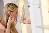 Young woman putting on earring in shop