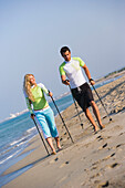 Couple walking with poles on beach, Apulia, Italy