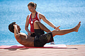 Female trainer helping man with stretching exercises, poolside, Apulia, Italy