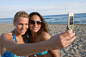 Two young woman on beach, taking picture with camera phone, Apulia, Italy