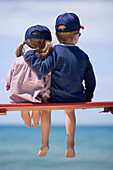 Zwei Kinder sitzen auf einer Bank am Strand, Apulien, Italien