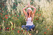 Young woman meditating on meadow with poppy flowers, Apulia, Italy