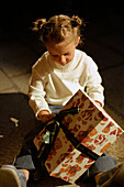 Girl (3-4 years) sitting on floor, holding christmas present