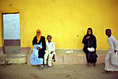 Egyptian people sitting in front of a yellow wall, Aswan, Egypt
