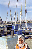 Egyptian girl standing in front of sailing boats at a harbour at the nile, Luxor, Egypt