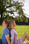 Couple sitting back to back on meadow