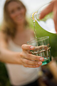Young woman holding glass, someone pouring water in