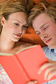 Junges Paar liegen auf Decke und lesen gemeinsam ein Buch