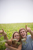 Young couple sitting on meadow, both pointing