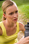 Junge Frau rastet beim Jogging, hält Wasserflasche