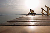 Young woman stretching on jetty before jogging