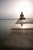 Woman meditating on jetty, lakeshore