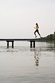 Junge Frau joggt auf einem Steg am See
