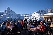 People sitting on the terrace of the Restaurant Blauherd with a view to the Matterhorn, Zermatt, Valais, Switzerland (2571 metres above sea level)