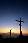 Mountaineer and cross on the summit of Heuberg at sunset with view to the Wendelstein range, Bavarian Alps, Upper Bavaria, Bavaria, Germany