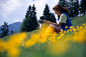 Hiker reading a map in a field of flowers, Raineralm, Kaiser range, Tyrol, Austria