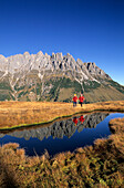 Two hikers at a lake on Hochkeil with view to Bratschenkopf, Manndlwand, Hochkoenig area, Berchtesgaden range, Salzburg, Austria