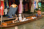 Female tourist in a wooden boat choosing a dress at a stand at Floating Market, Damnoen Saduak, near Bangkok, Ratchaburi, Thailand