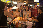 People standing around a food stand at Th Khao San Road in the evening, Banglamphu, Bangkok, Thailand