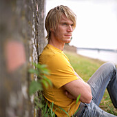 Young blond man leaning against wall at rivershore