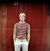 Young blond man standing in front of rusty background