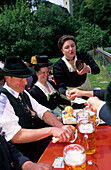 young women in dirndl dresses and young men in traditional dresses in beer garden, waitress receiving money, pilgrimage to Raiten, Schleching, Chiemgau, Upper Bavaria, Bavaria, Germany