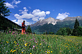 Hiker in a field of flowers and view to Sassalb Mountain Range, Puschlav, Grisons, Switzerland