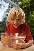 Junge beugt sich über eine Schüssel mit Wasser und einem Apfel, Kindergeburtstag