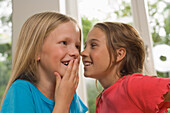 Girl whispering into girlfriend's ear, children's birthday party