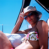 Frau in Bikini mit Sonnenbrille und Hut sitzt auf einem Segelboot und blickt in die Kamera, Dalmatien, Kroatien