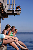 Three girls jumping off into the lake from a wooden diving platform, Utting, Ammersee, Bavaria, Germany