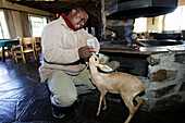 Ein Angestellter der Lodge füttert eine Baby Antilope mit Milch aus der Flasche. Canon Lodge, Gondwana Canon Park. Fish River Canyon, Südliches Namibia, Afrika