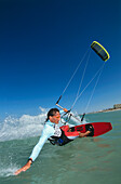 Man kiteboarding, holding hand into water